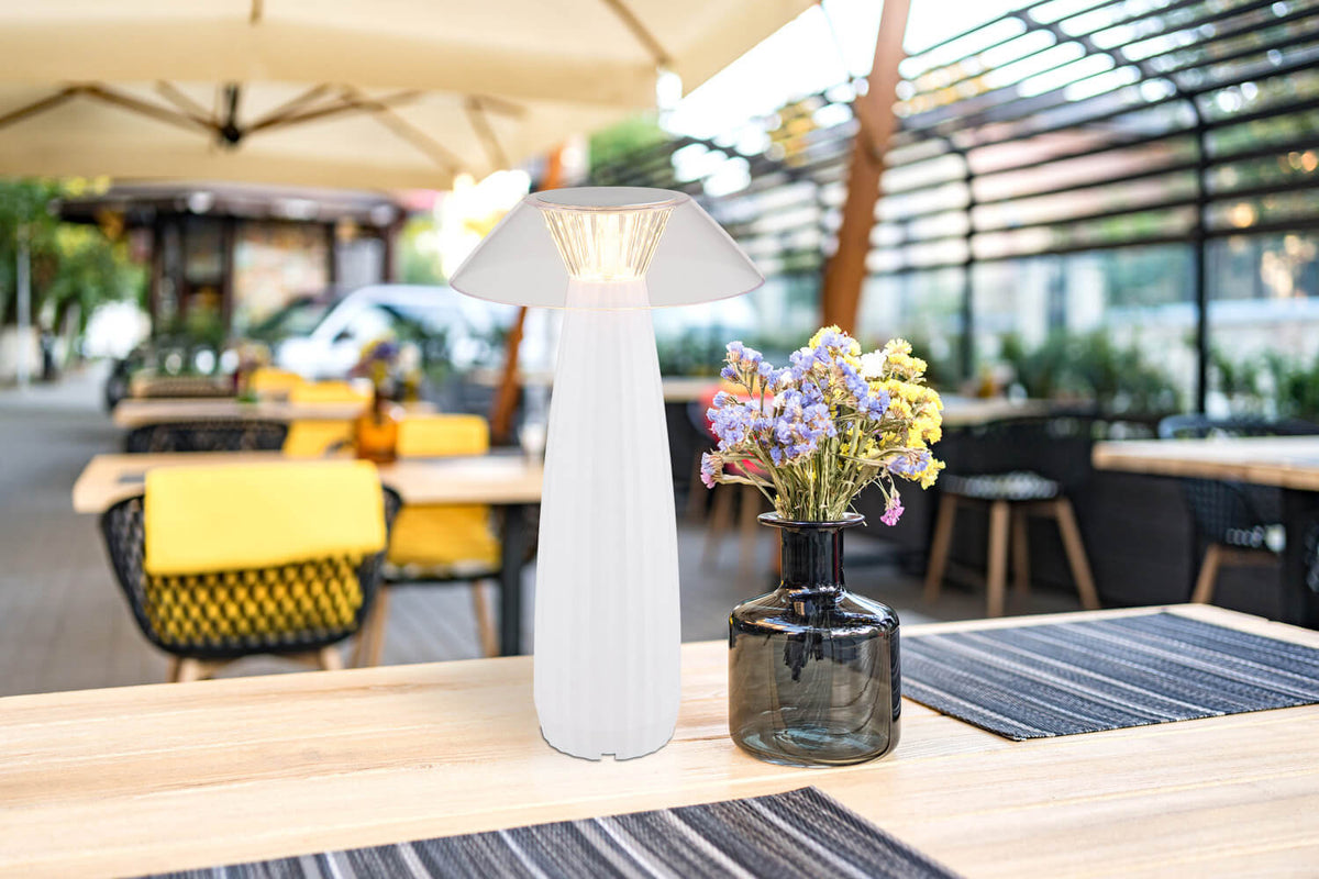 Mise en ambiance : lampe posée sur une table de terrasse, près d'un vase de fleurs séchées
