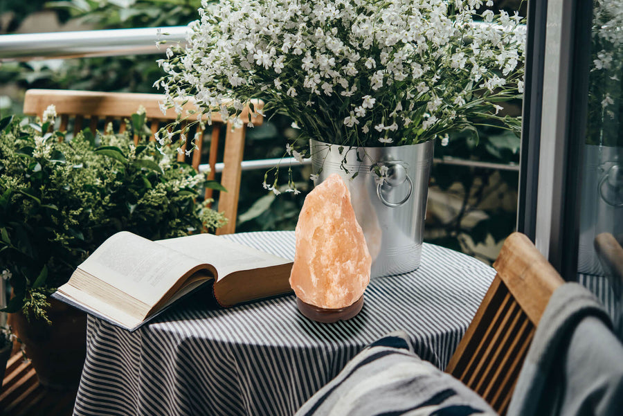 Lampe en sel posée sur une table de balcon, livre ouvert et fleurs blanches
