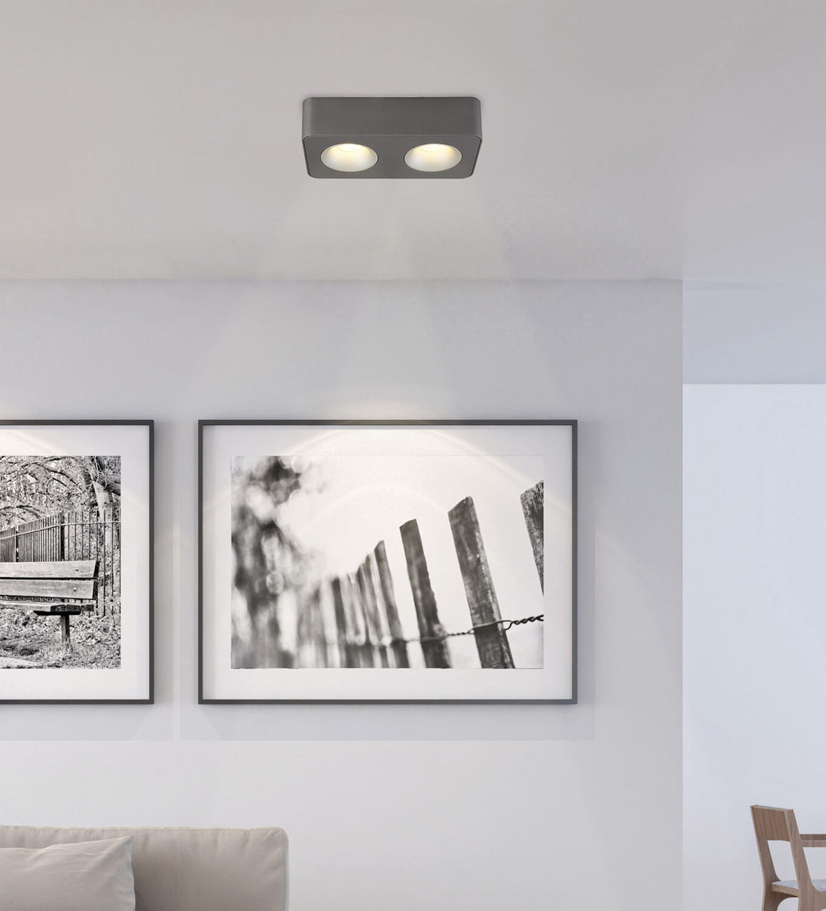 Mise en ambiance : spot double fixé au plafond éclairant des cadres photo dans un salon