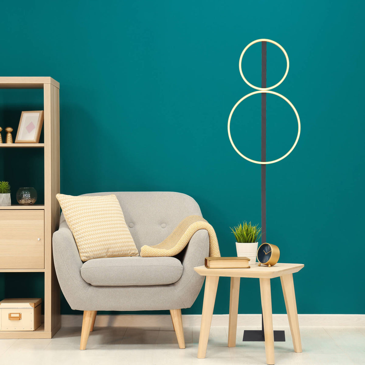 Mise en ambiance : lampadaire allumé devant un mur turquoise, fauteuil et table basse