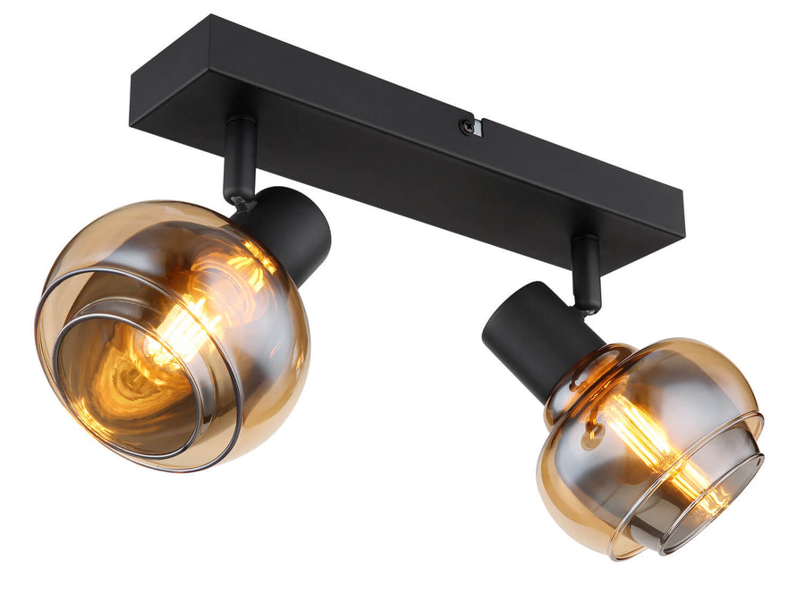 Vue en légère contre-plongée du luminaire allumé, montrant les deux têtes orientables et leur verre fumé.
