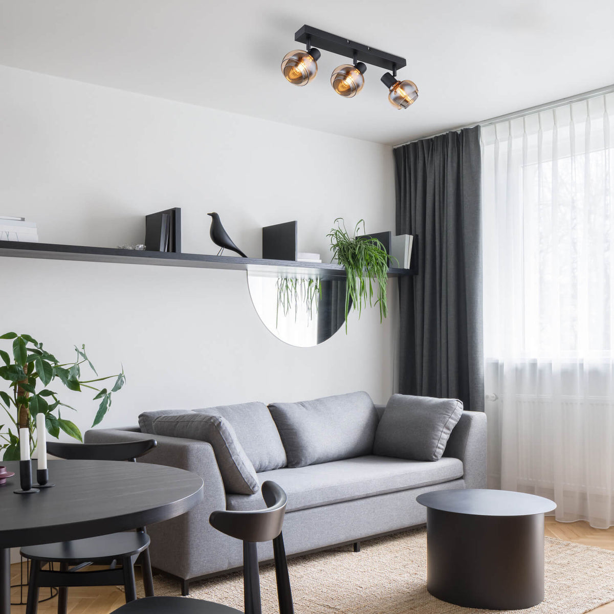 Mise en ambiance dans un salon, plafonnier allumé au-dessus du canapé gris.