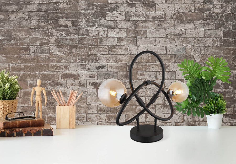 Lampe posée sur un bureau blanc devant un mur de briques, avec plantes et livres.