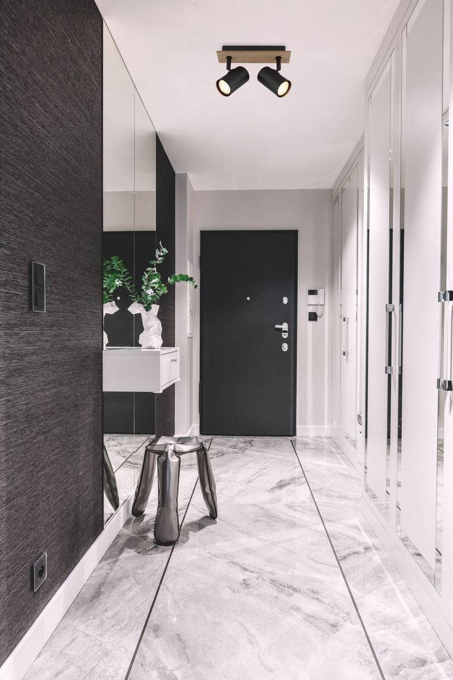 Entrée moderne avec plafonnier double spot noir éclairant le couloir, porte noire et sol marbre.