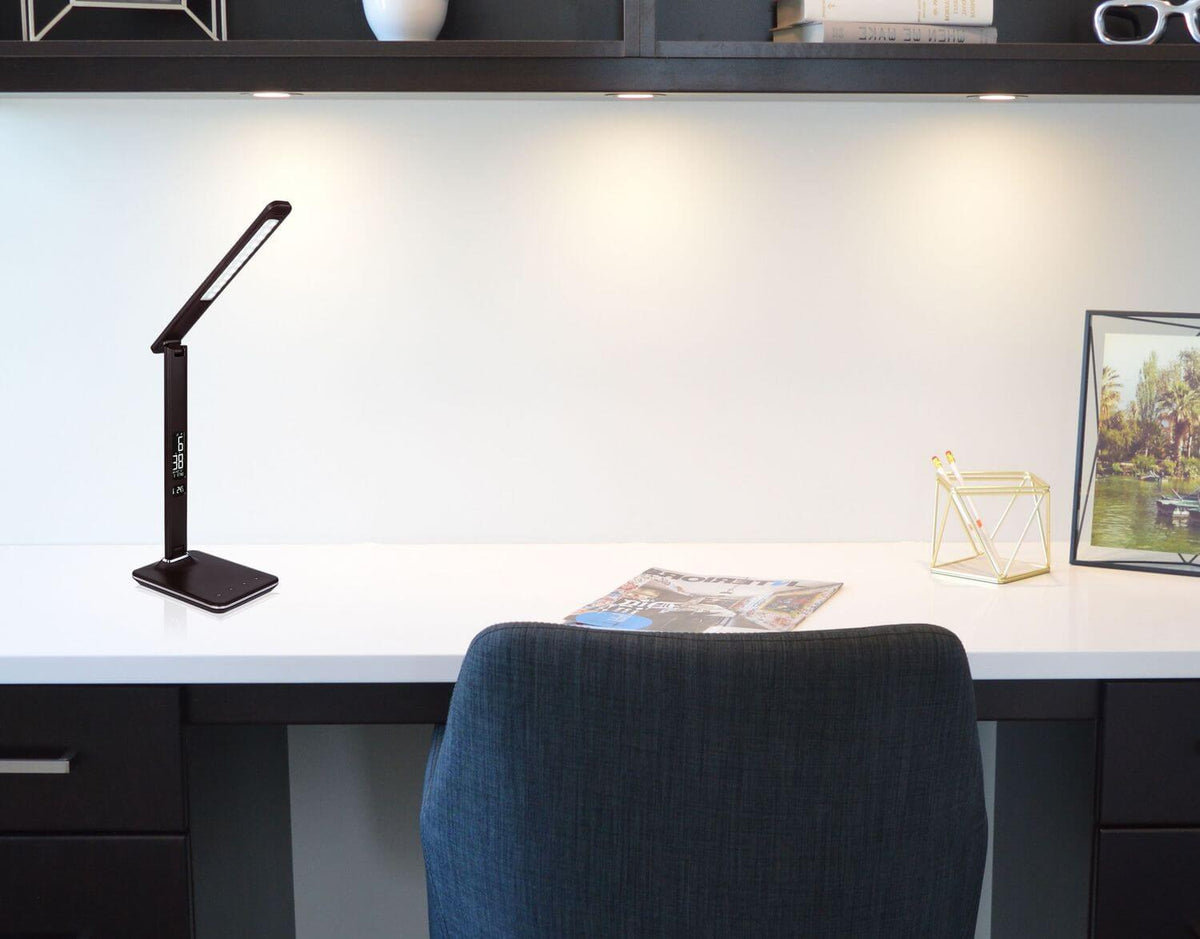 Mise en ambiance sur un bureau blanc, lampe allumée près d'une chaise et d'étagères.