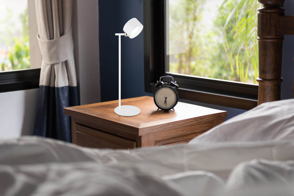 Mise en ambiance dans une chambre, lampe allumée sur une table de chevet.