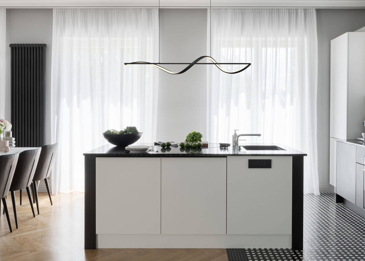 Mise en ambiance au-dessus d'un îlot de cuisine, luminaire suspendu noir ondulé allumé.