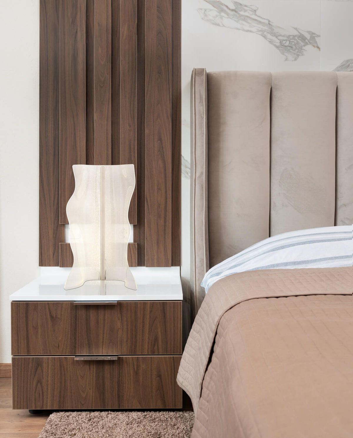 Mise en ambiance sur une table de chevet, luminaire allumé près d'un lit