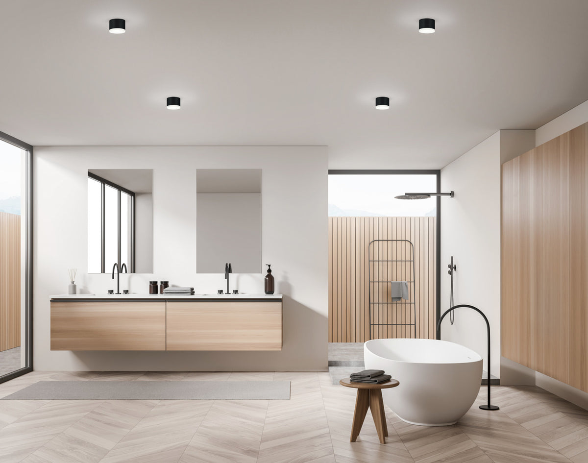 Vue large de la salle de bain en bois clair équipée des mêmes plafonniers cylindriques.