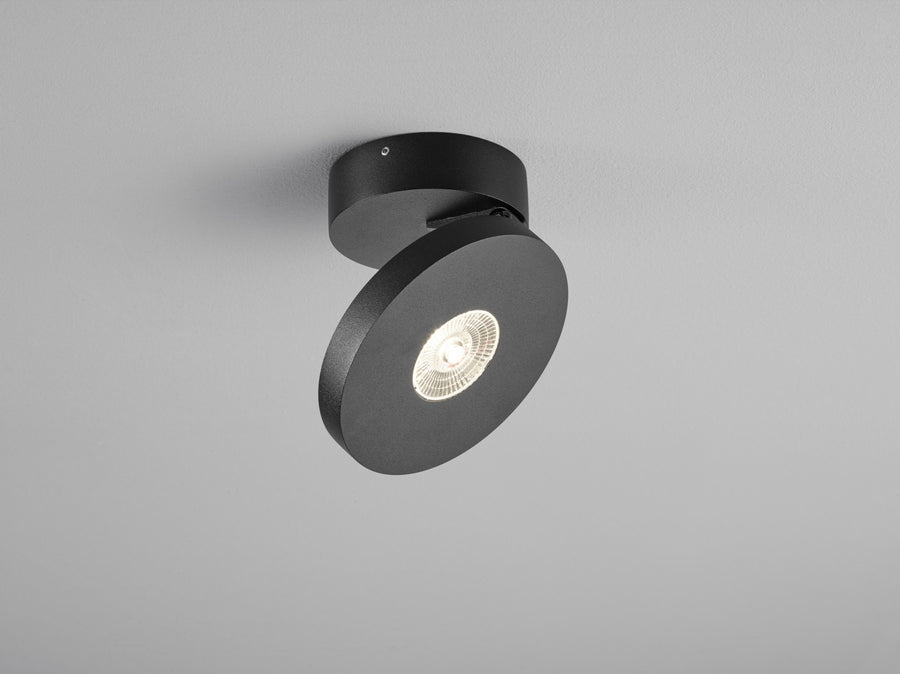 Plafonnier noir orientable vu de trois quarts, spot LED allumé au centre