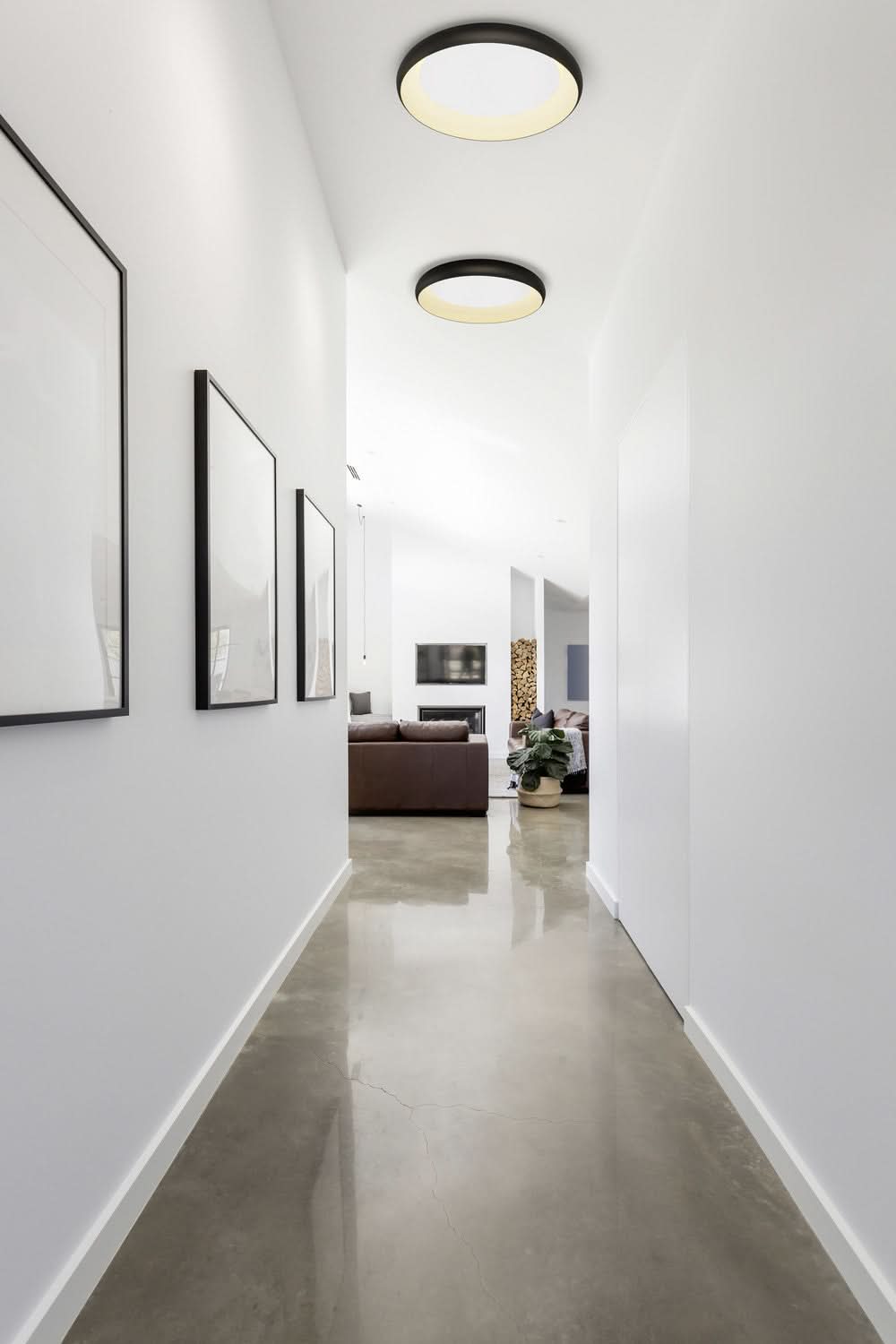 Couloir contemporain, plafonniers noirs ronds au plafond, sol béton ciré et cadres muraux