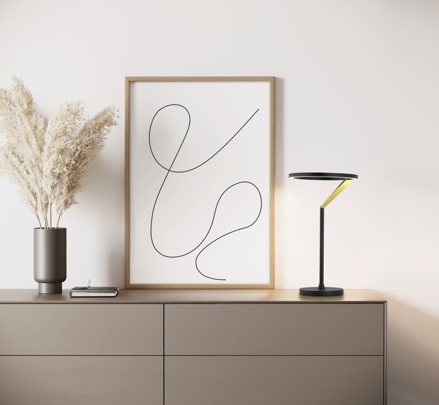 Lampe posée sur une commode beige devant un cadre et un vase de pampas