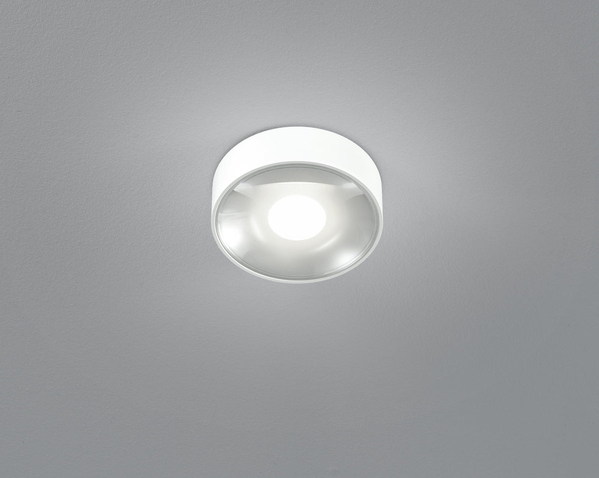 Vue de dessous du plafonnier blanc allumé, diffuseur en verre bombé et halo lumineux