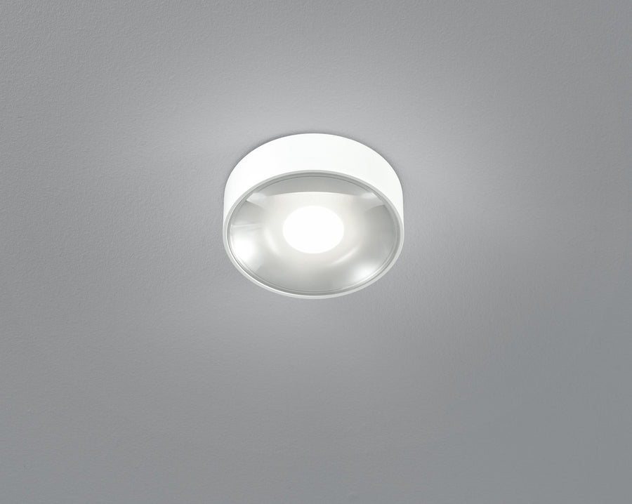 Vue de dessous du plafonnier blanc allumé, diffuseur en verre bombé et halo lumineux