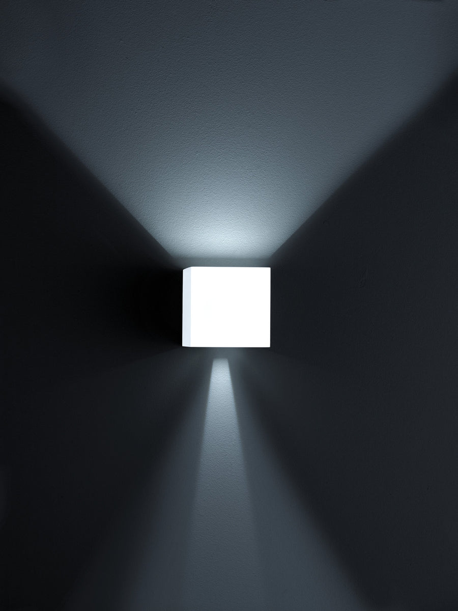 Applique murale cube blanche allumée seule dans la pénombre, éclairant vers le haut et le bas