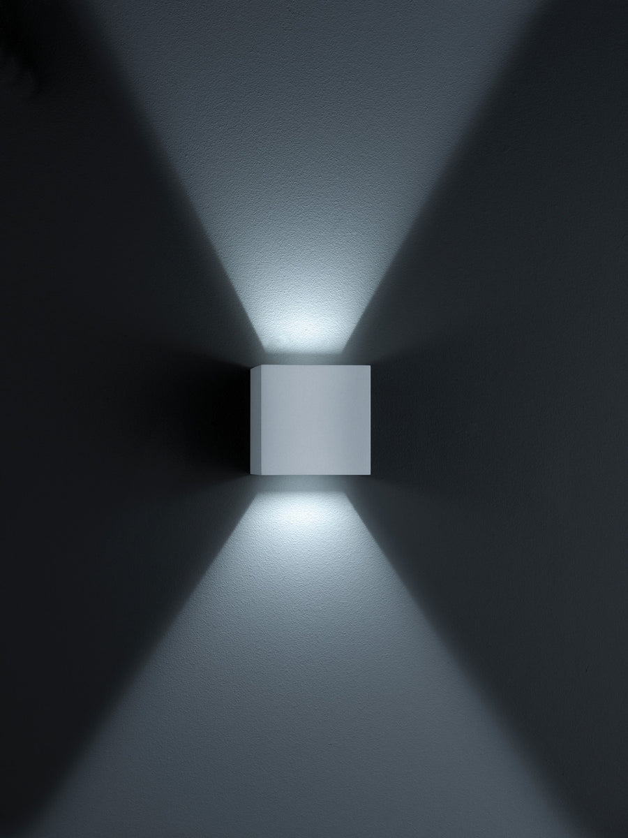 Applique cubique grise sur mur sombre projetant deux cônes lumineux verticaux