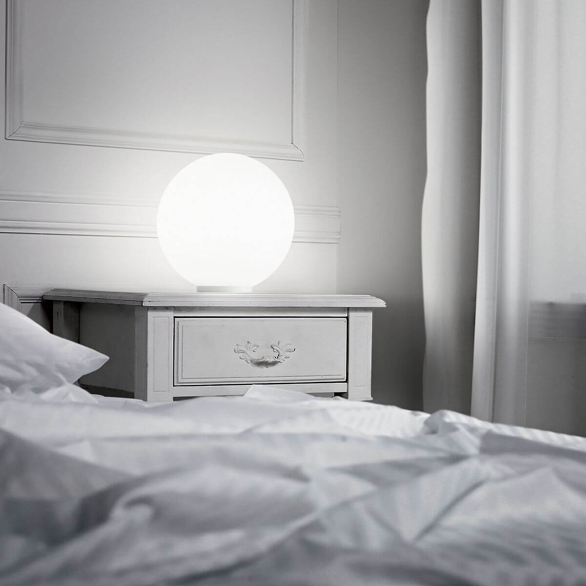 Lampe sphérique allumée posée sur table de chevet dans une chambre