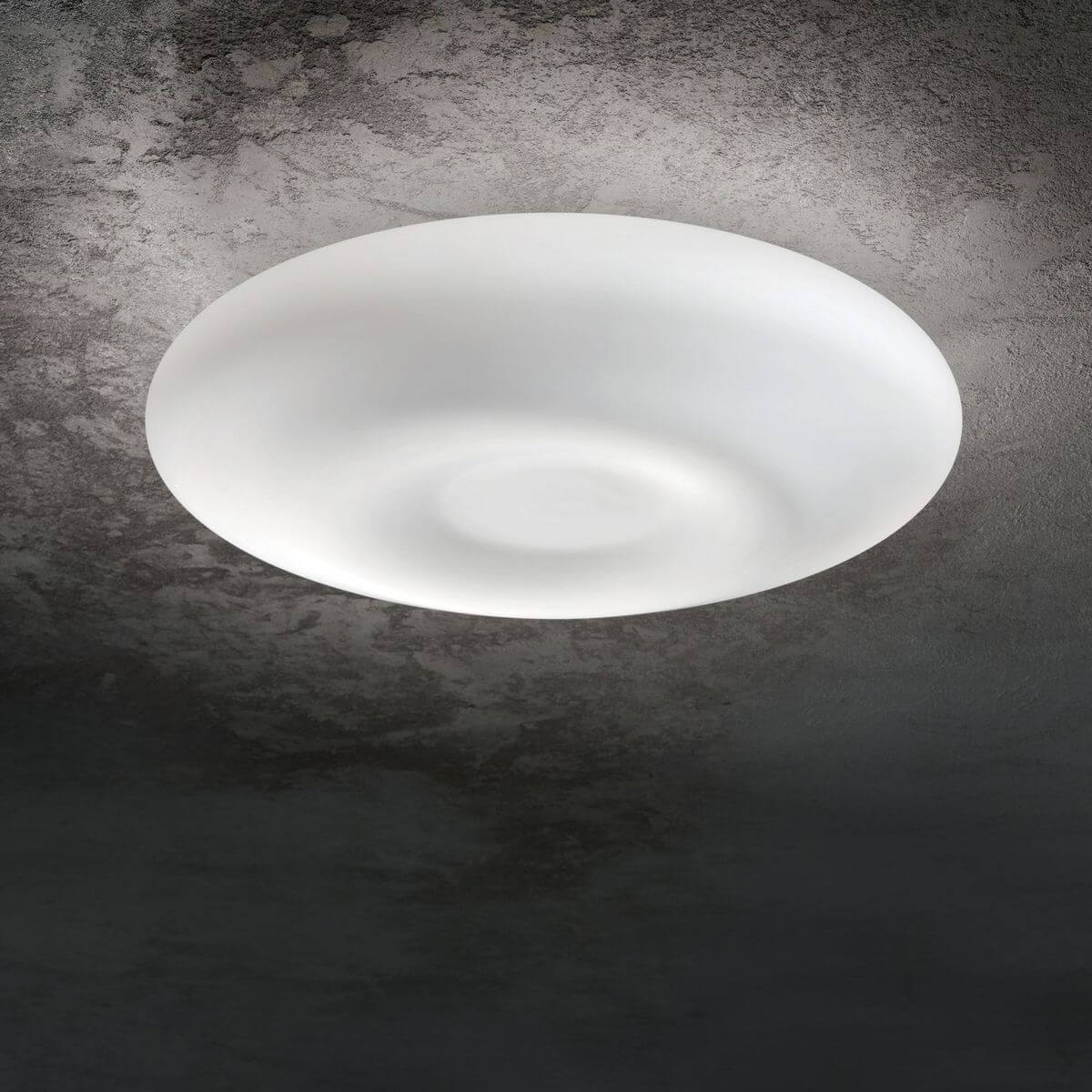 Diffuseur blanc allumé fixé au plafond, halo lumineux sur béton gris texturé