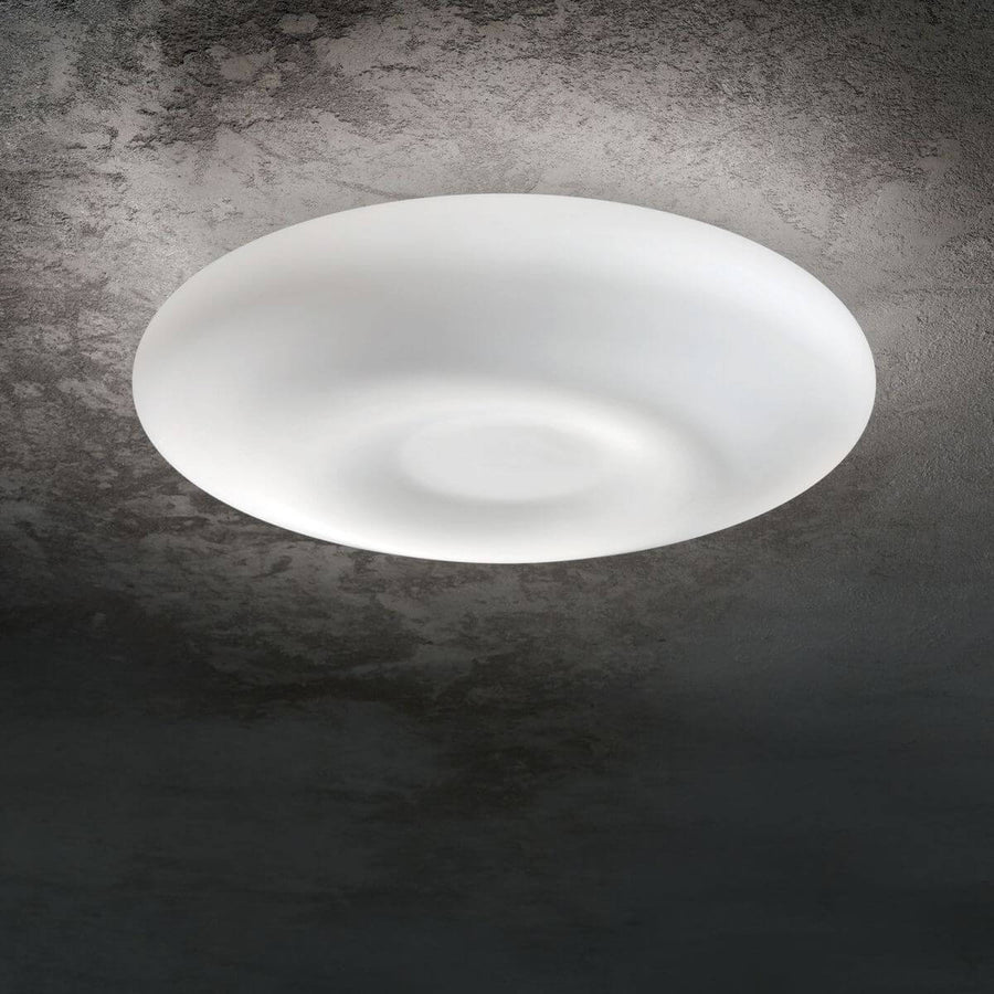 Plafonnier rond en verre blanc allumé, fixé au plafond en béton brut