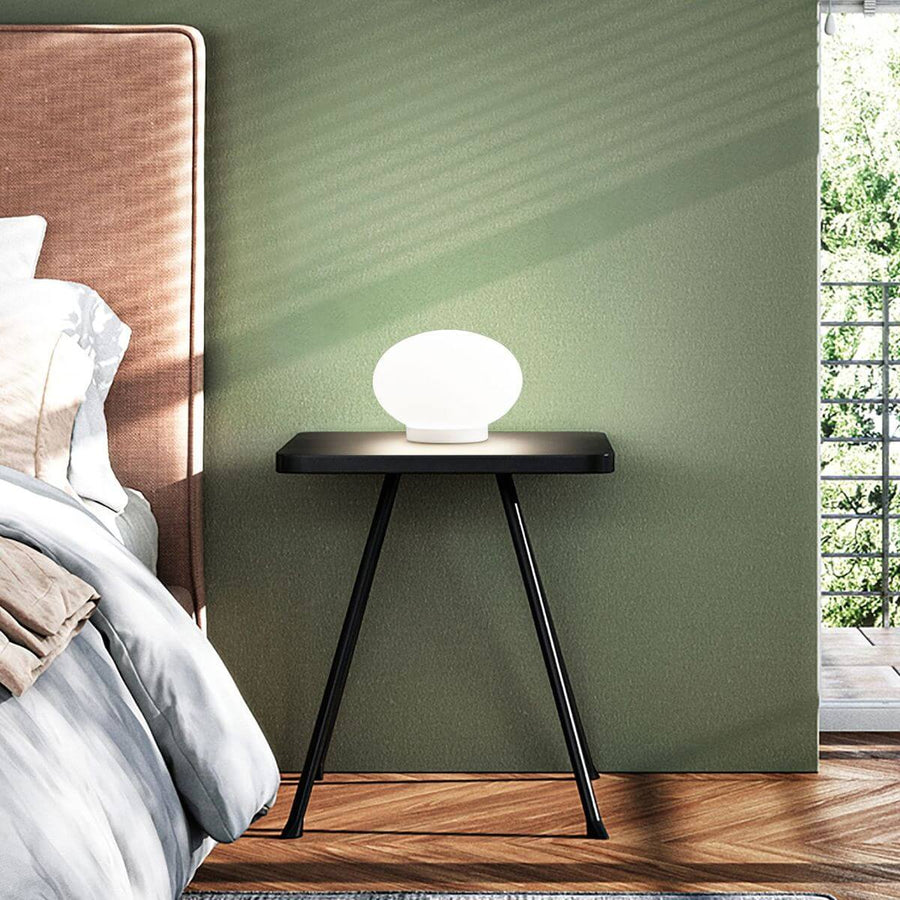 Lampe blanche allumée posée sur une table de chevet noire dans une chambre