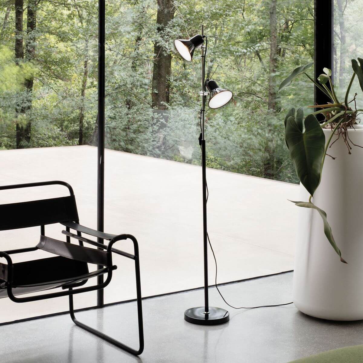 Lampadaire noir installé dans un salon vitré face à la forêt, mise en ambiance