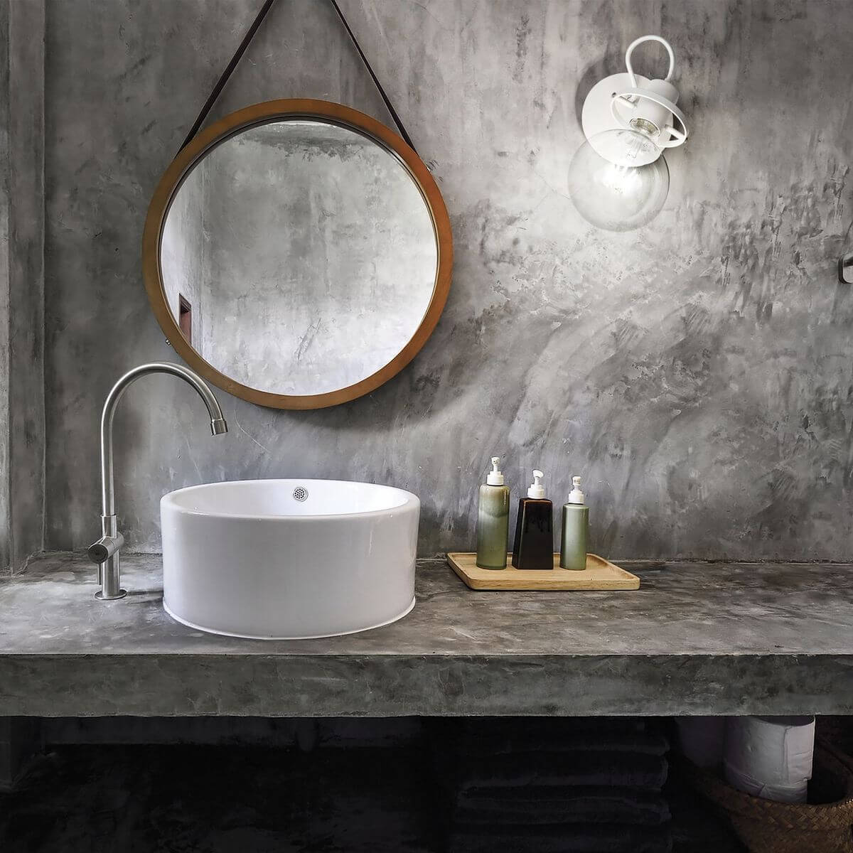 Mise en ambiance dans une salle de bain béton gris, miroir rond et vasque blanche
