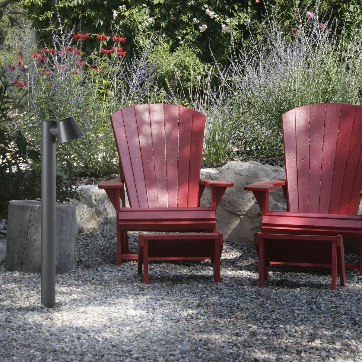 Lampadaire extérieur anthracite installé dans un jardin près de fauteuils rouges sur gravier
