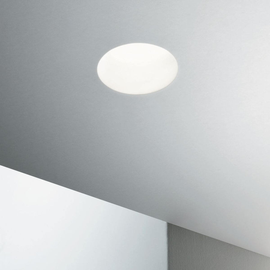 Luminaire encastré allumé dans un plafond blanc, halo lumineux diffus.
