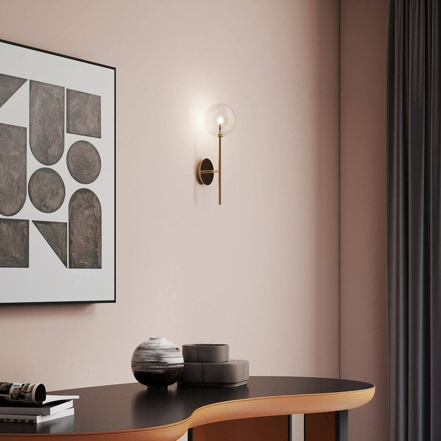 Applique murale laiton éclairée sur un mur rose pâle au-dessus d'une console.