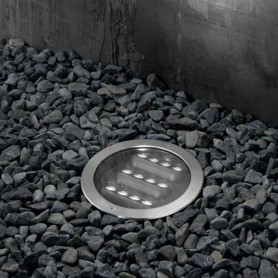 Luminaire encastré dans un lit de galets gris, éclairé et vu de face