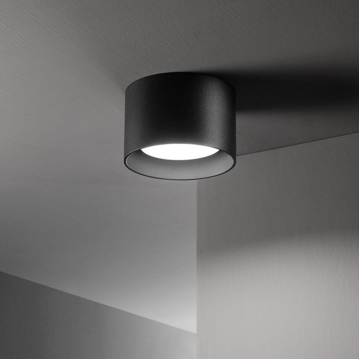 Luminaire noir installé au plafond dans une pièce, halo lumineux projeté sur le mur
