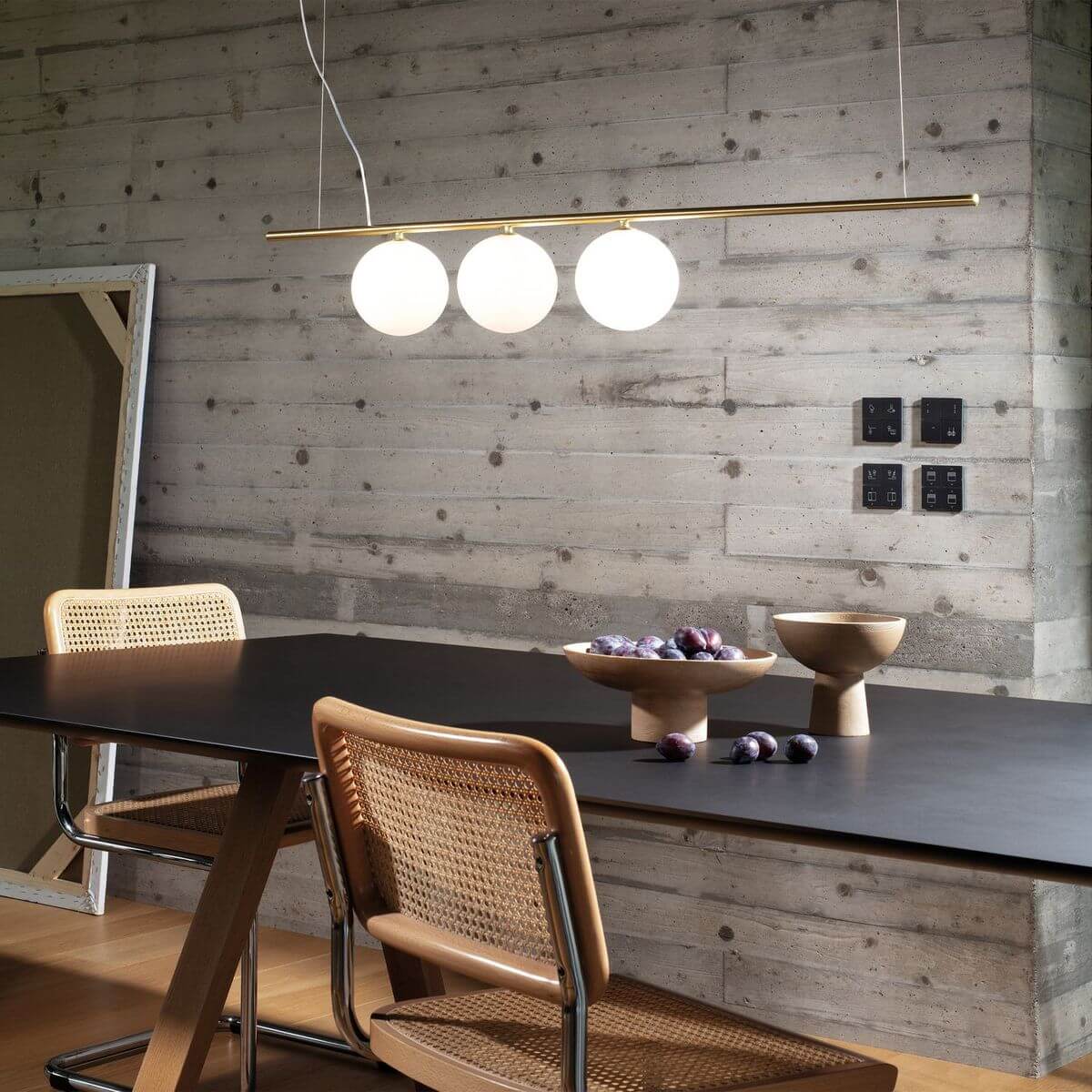 Suspension allumée au-dessus d'une table noire dans une salle à manger béton, ambiance contemporaine.