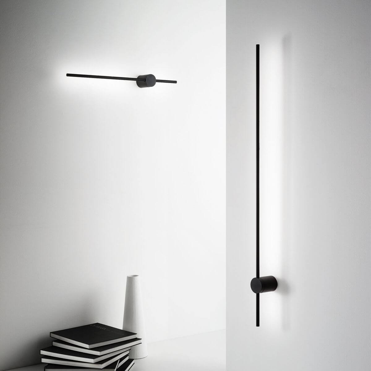 Mise en ambiance sur mur blanc, deux appliques linéaires noires éclairant le mur.