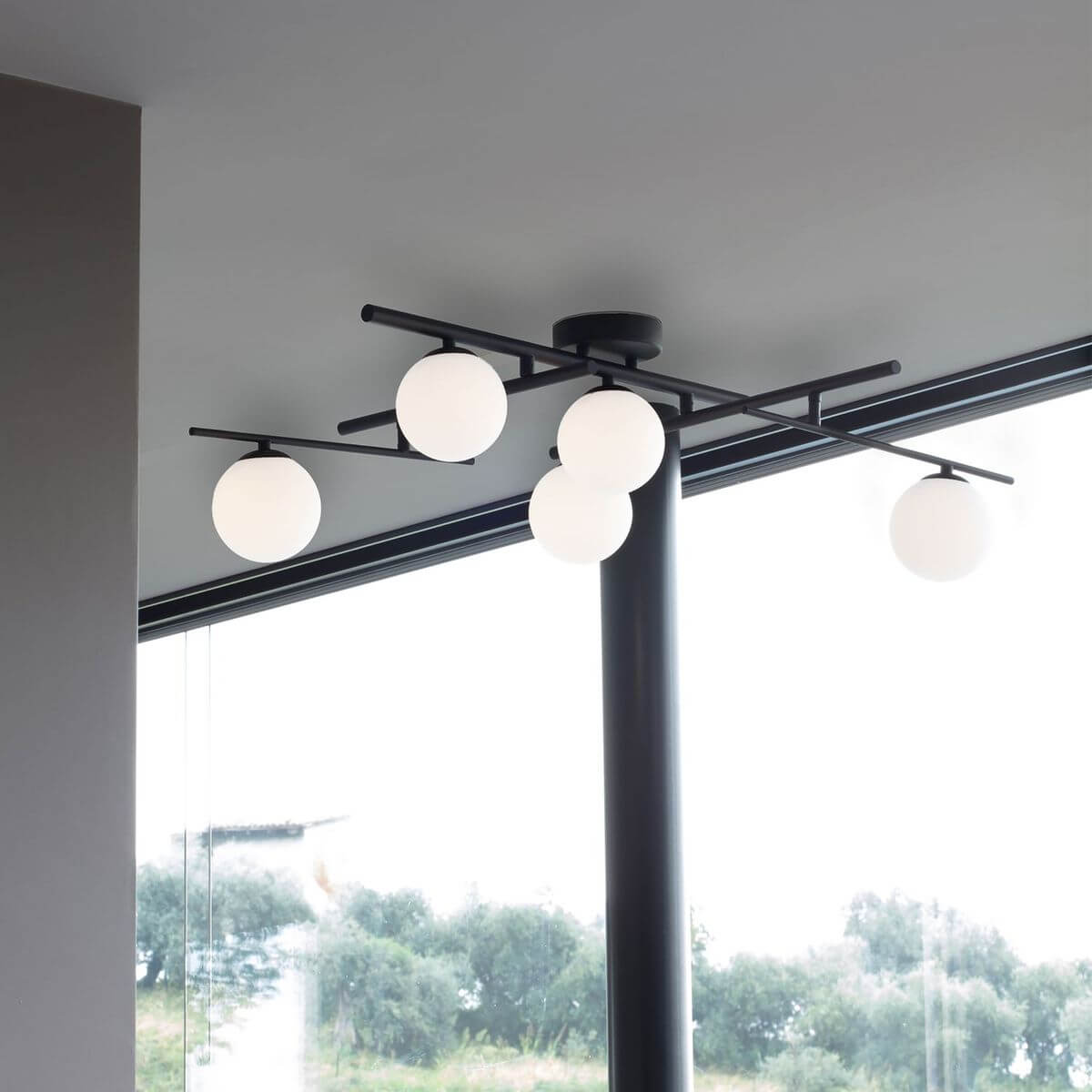 Plafonnier noir à cinq globes, installé au plafond près d'une baie vitrée.