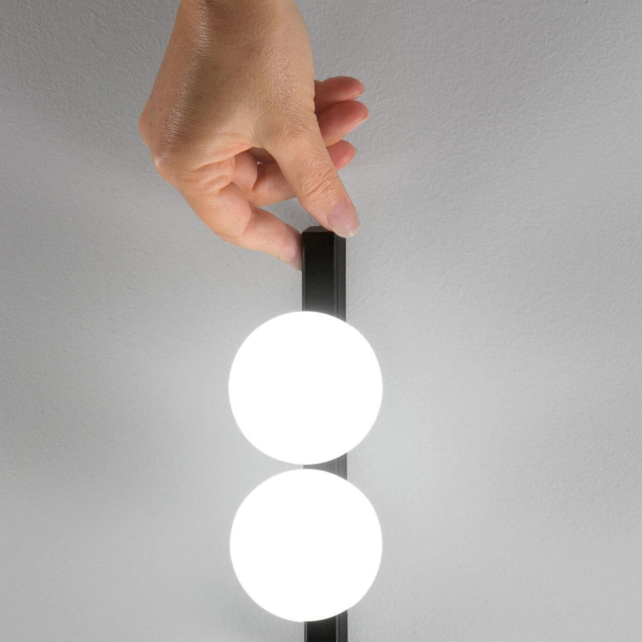 Main ajustant la tige noire, détail des globes de verre opalin allumés.