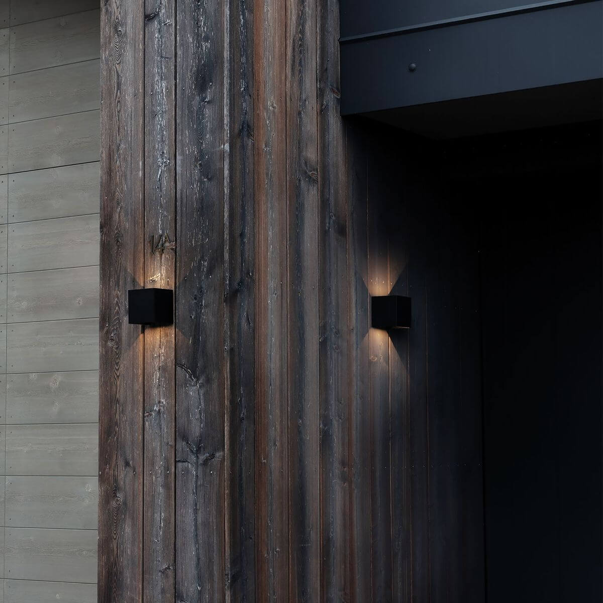 Mise en ambiance extérieure : deux appliques cubes noires sur bardage bois sombre