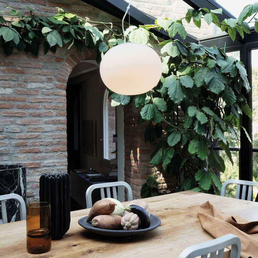 Suspension allumée au-dessus d'une table en bois dans un intérieur avec mur de briques et plantes.