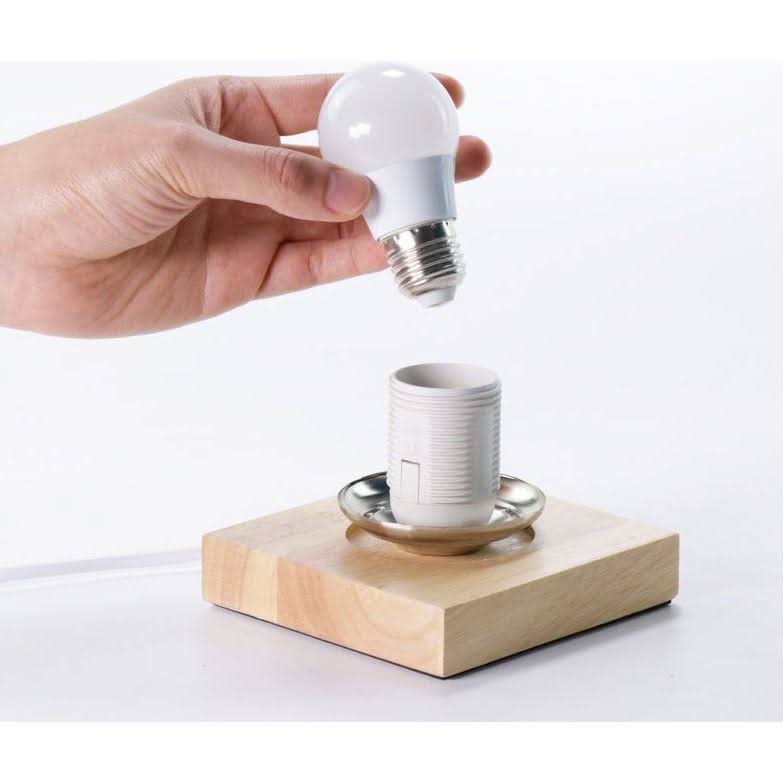 Détail de la base en bois avec douille E27 et ampoule LED tenue à la main.