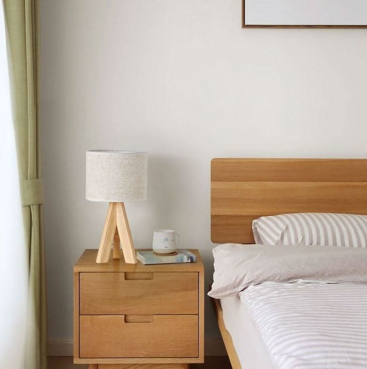 Lampe allumée sur chevet en bois près d'un lit, ambiance chambre cosy