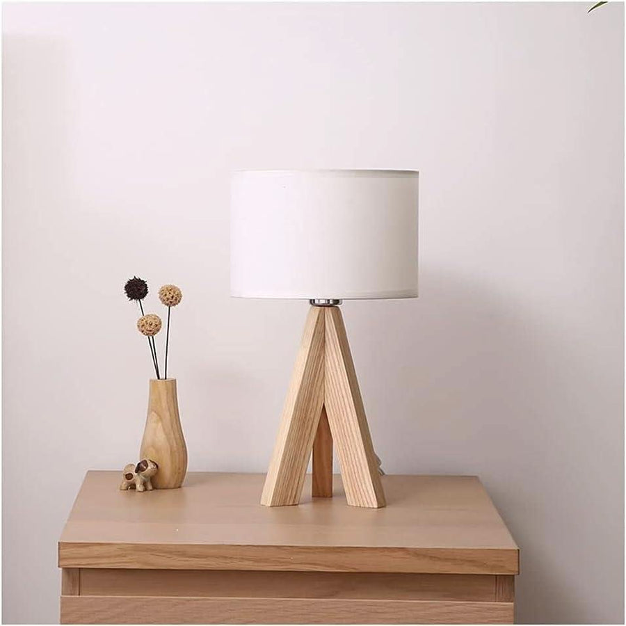 Lampe blanche sur table de nuit en bois, vase de fleurs séchées à gauche