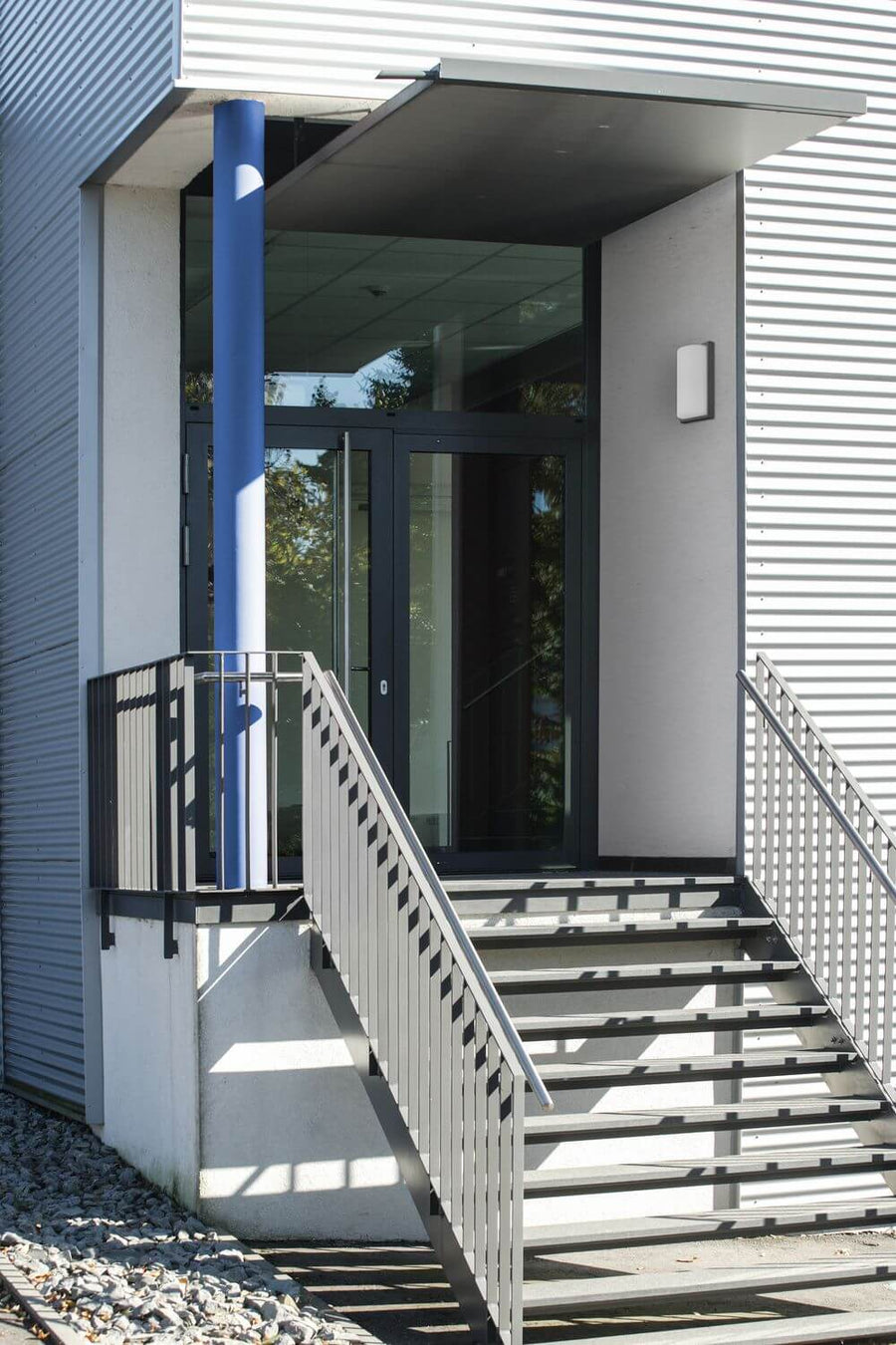 Applique anthracite installée sur mur blanc près d'une entrée moderne avec escalier.