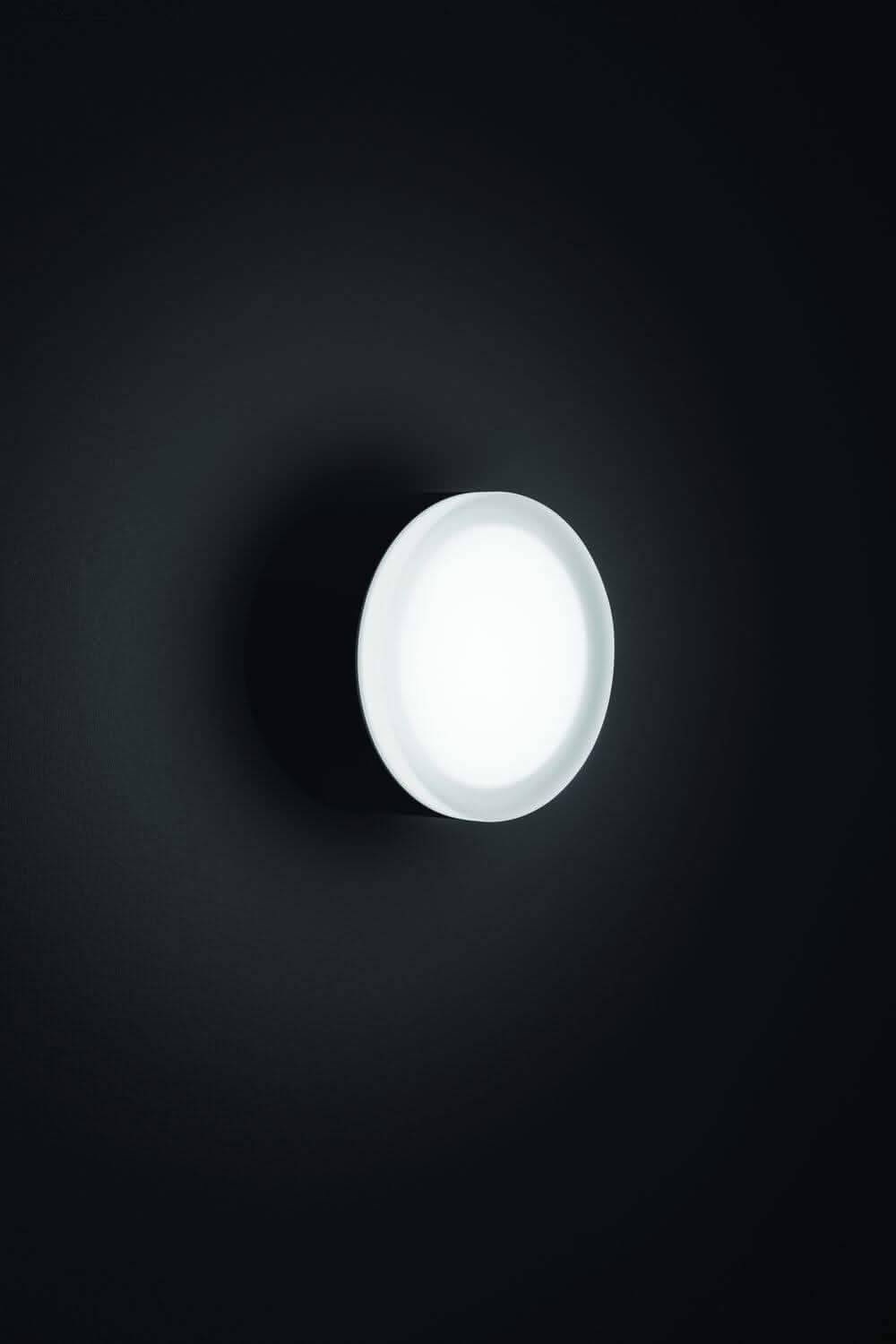 Diffuseur blanc allumé dans l'obscurité, halo lumineux sur un mur sombre