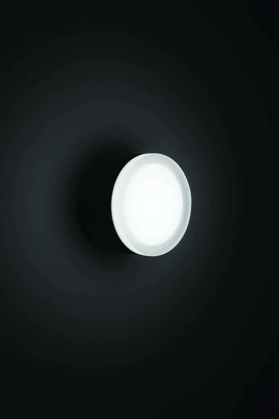 Diffuseur blanc allumé dans l'obscurité, halo lumineux sur un mur sombre