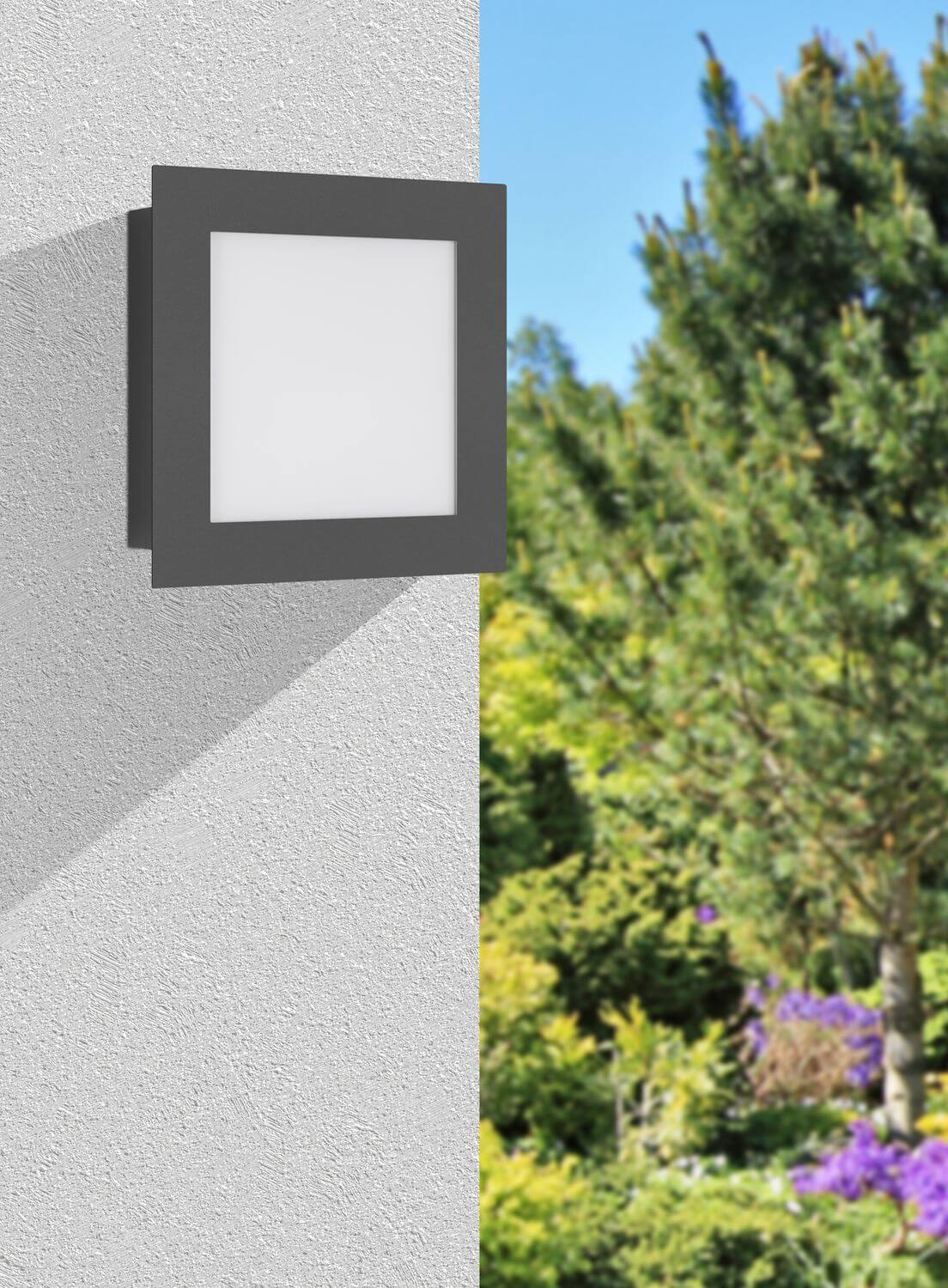 Applique carrée anthracite installée sur une façade claire, jardin verdoyant en arrière-plan