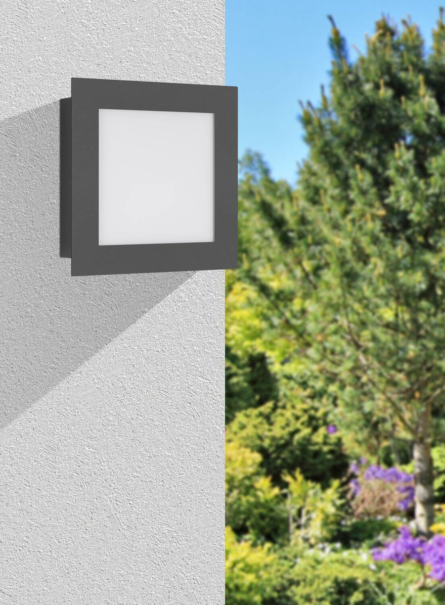 Applique carrée anthracite installée sur une façade claire, jardin verdoyant en arrière-plan