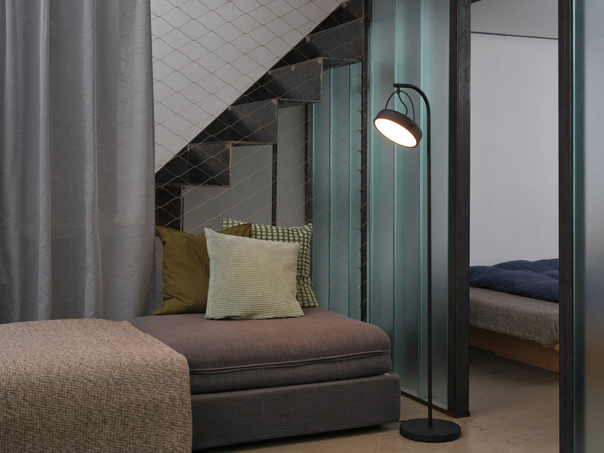 Lampadaire allumé dans un salon contemporain près d'un canapé et d'un escalier.