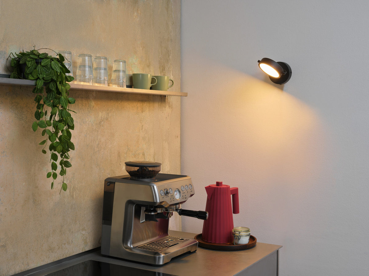 Mise en situation de l'applique murale noire éclairant un plan de travail avec machine à café.