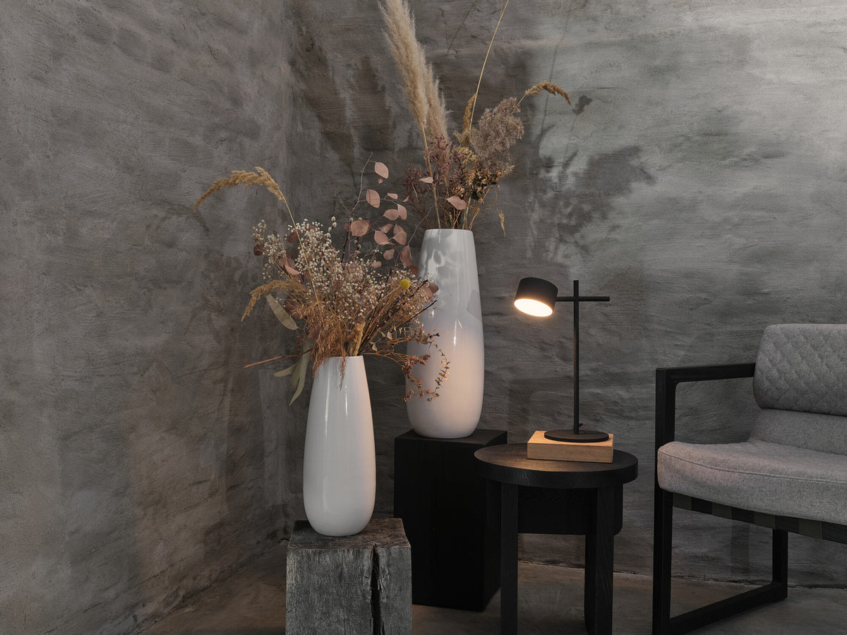 Mise en ambiance : lampe allumée sur table basse près d'un fauteuil et vases.