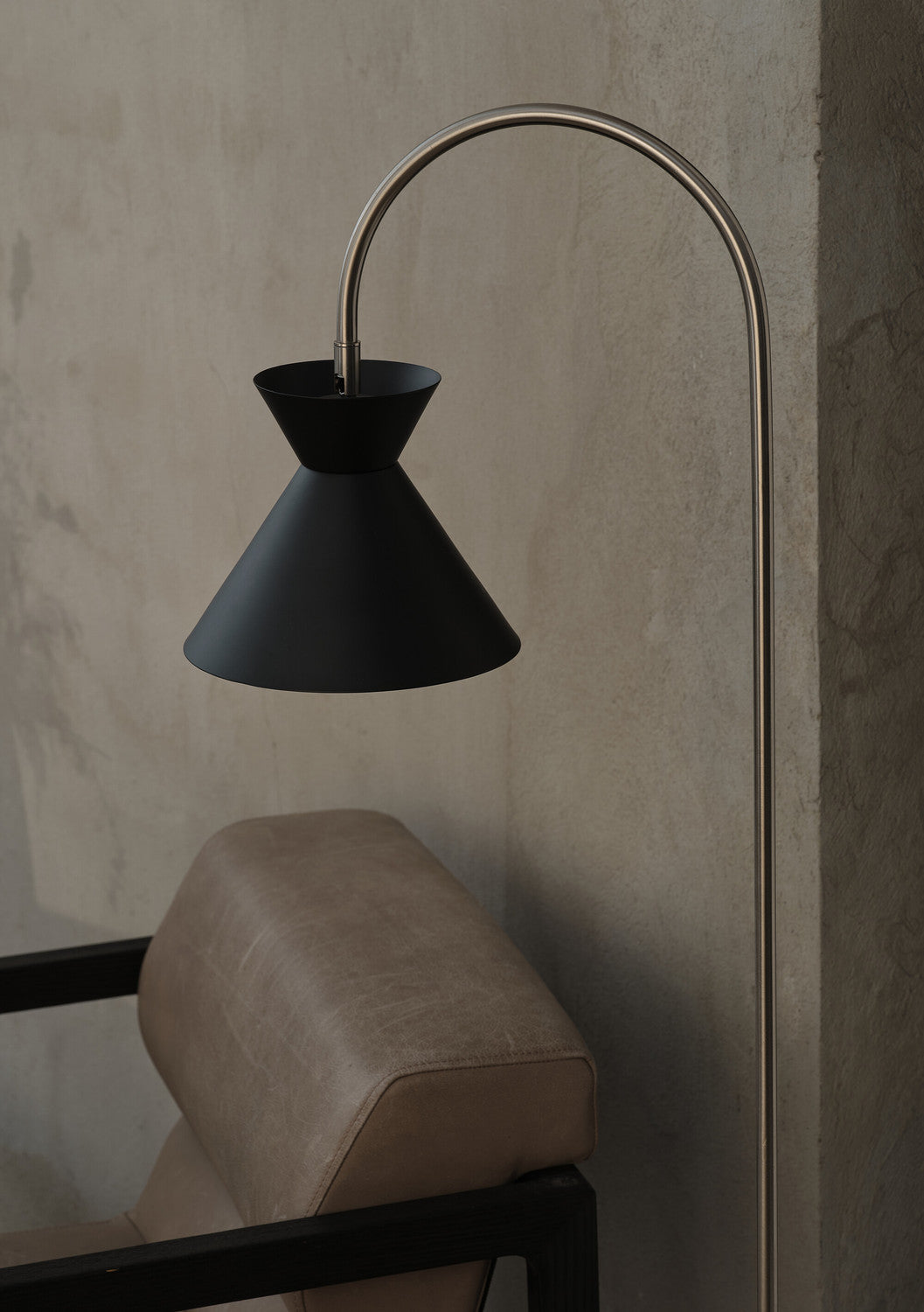 Détail rapproché de l'abat-jour conique noir au-dessus d'un fauteuil beige.