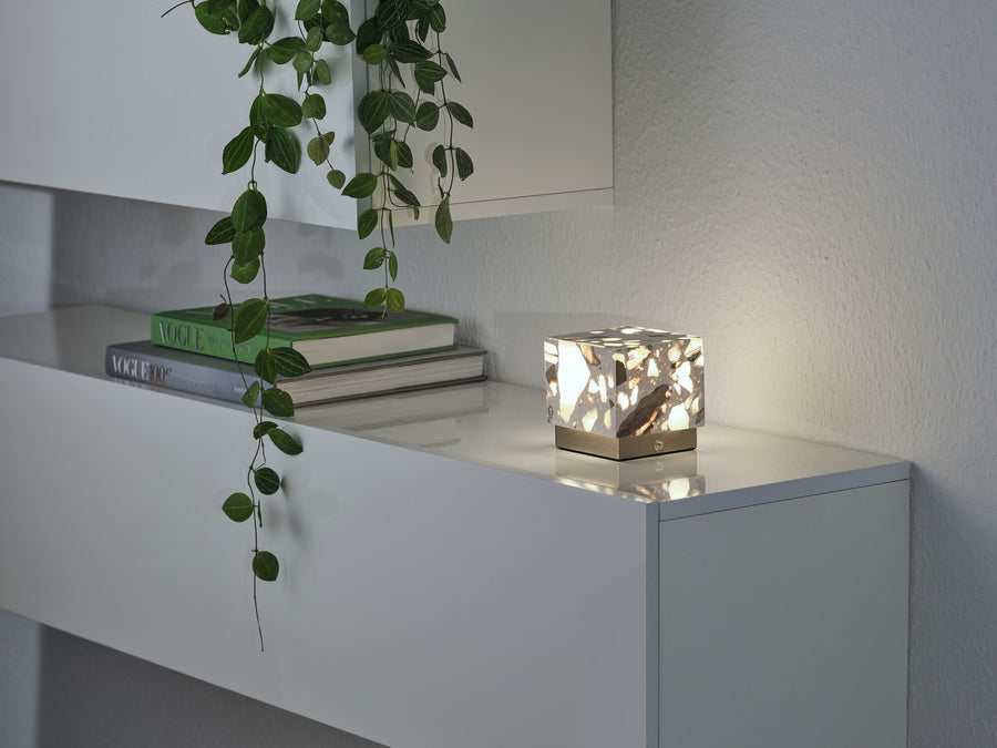 Scène répétée du luminaire allumé sur l'étagère, avec livres empilés et plante retombante.
